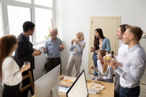 Syv kollegaer står rundt et bord og spiser og snakker sammen.